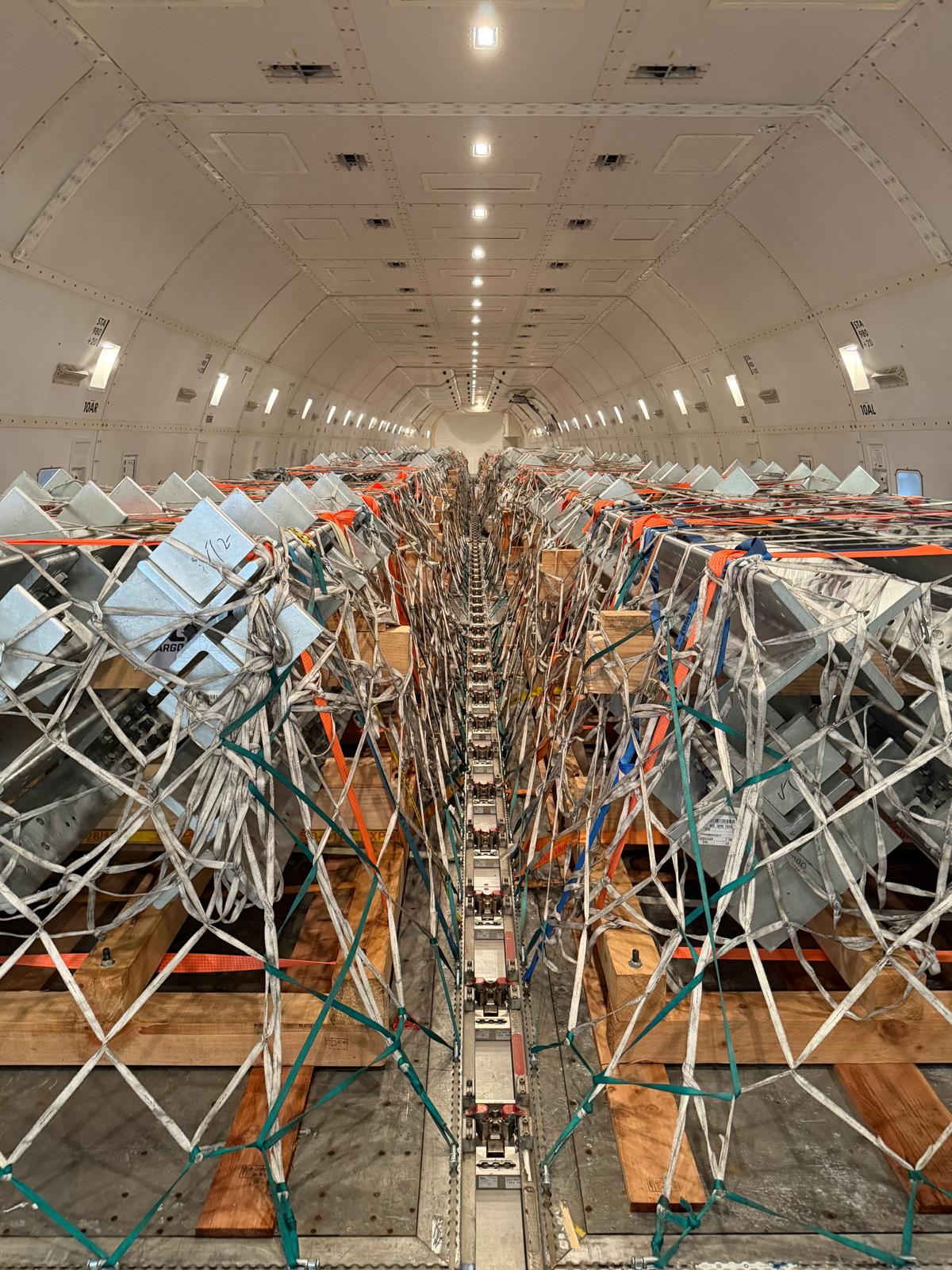 Loaded freighter main deck with crated industrial cargo on pallets secured under nets and strapping